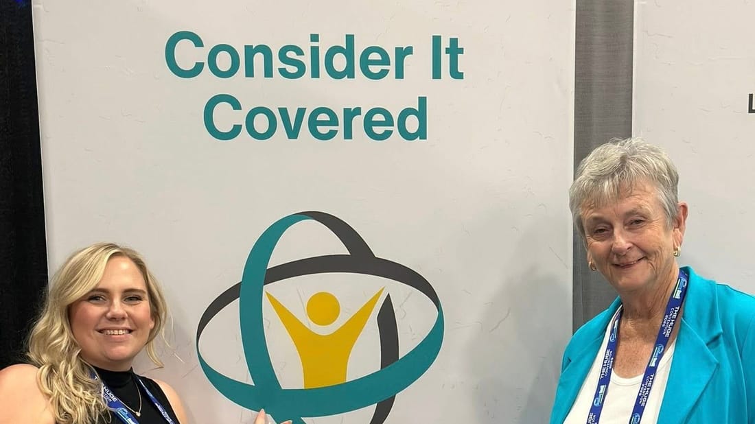 Two members of the Contractor In Charge team beside the company's Consider It Covered trade-show sign